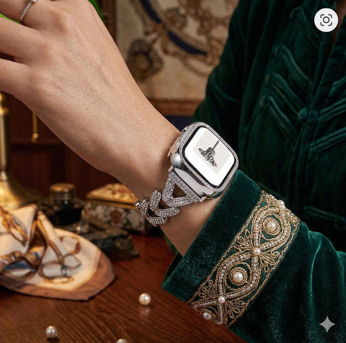 May include: A silver smartwatch with a diamond-encrusted strap and case. The watch face shows a black and white image. The strap has a leaf design. The person is wearing a green velvet jacket with gold embroidery.